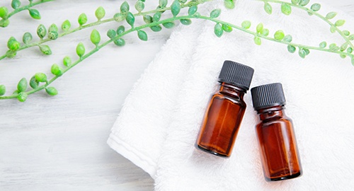 Essential oils in brown bottles on a white towel with decorative greenery