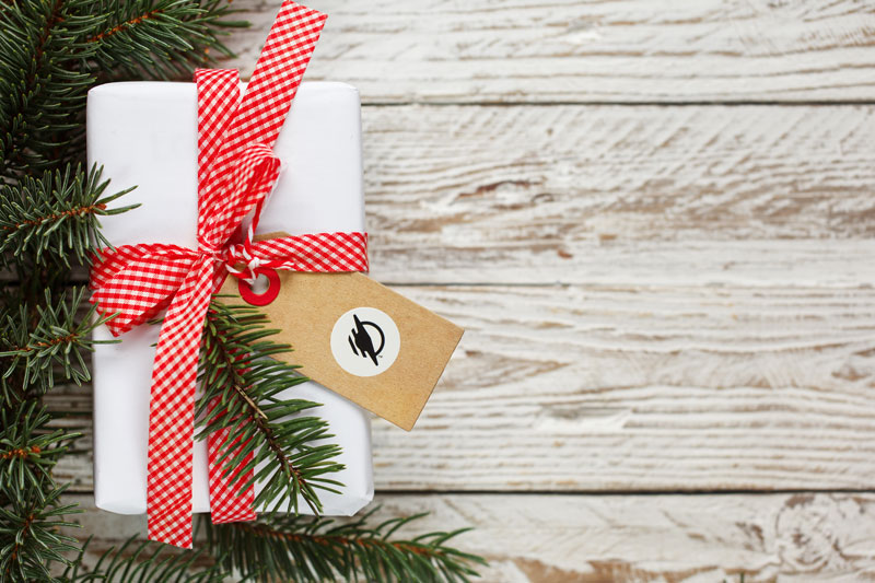 Photo of a present with a WayTag on the nametag. There is the edge of a Christmas tree to the left of the present.