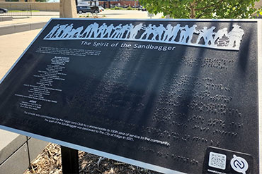 A park sign with a relief of people at the top, text on the right and brail on the left.