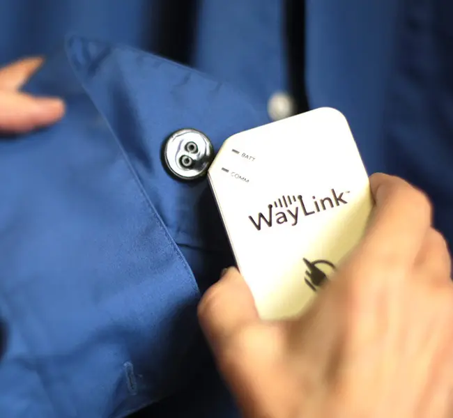 A person holding a WayLink reader up to one of the WayTag 2-hole Buttons on a dark blue long sleeve shirt.
